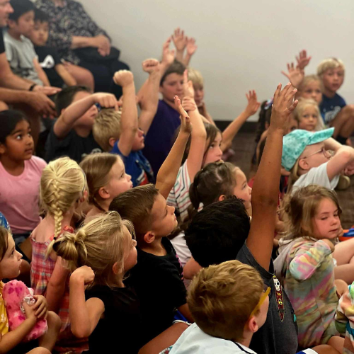 children seated raising their hands in a library program.